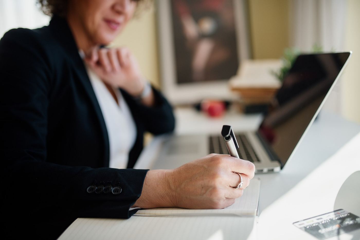 Profissional de terno tomando notas numa mesa de trabalho, ao lado de um notebook